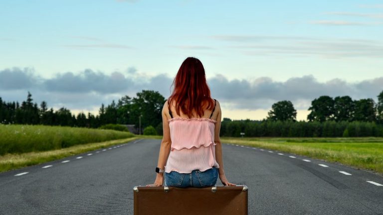 Woman sitting on suitcase in countryside, symbolizing travel and freedom.